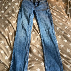 Blå jeans med raka ben - Säljer ett par klassiska blå jeans med raka ben och femficksdesign. De har en ljus tvätt och en läderpatch baktill i midjan. Perfekta för en avslappnad stil.