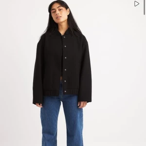 Svart bomberjacka - Snygg svart bomberjacka med knappar framtill. Jackan har en klassisk design med långa ärmar och en rak passform. Perfekt för en stilren look.