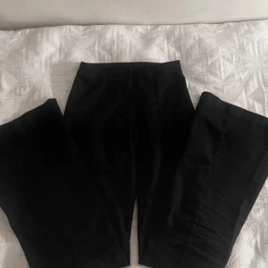 Svarta kostymbyxor högmidjade från Monika - Snygga svarta kostymbyxor med hög midja och rak passform. Perfekta för en stilren look. De är tillverkade i ett mjukt och bekvämt material som ger en elegant känsla. FRÅN MONKI