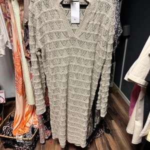 Beige stickad klänning från Stajl - Säljer en snygg beige stickad klänning från Stajl med v-ringning och ett fint mönster. Perfekt för kyligare dagar med sin långa ärm och mjuka material. Passar bra till både vardag och speciella tillfällen. Ord.Pris: 899 kr.