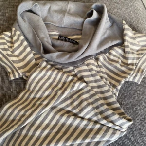 Randig kortärmad topp från Zara - Säljer en stilren randig topp från Zara med korta ärmar och en bred krage. Toppen har ett grått och beige mönster och en knappdetalj på ärmen. Perfekt för en avslappnad look.