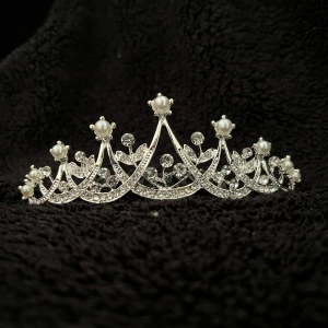 Silverfärgad tiara med pärlor - Elegant tiara i silverfärg med vackra pärldetaljer. Perfekt för speciella tillfällen med en stilren och glittrig design. Tiaran har en kam för enkel fastsättning i håret.