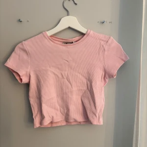 Rosa ribbad croppad topp - Säljer en söt rosa ribbad croppad topp med korta ärmar. Perfekt för sommardagar och att matcha med höga jeans eller kjol. Enkel och stilren design som passar till många tillfällen.