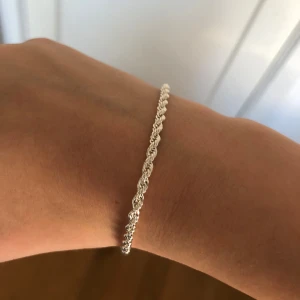 Silverfärgat armband - Elegant silverfärgat armband med tvinnad design. Perfekt för att lägga till en subtil glans till din outfit. Passar bra till både vardag och festliga tillfällen. Den är 20 cm lång 