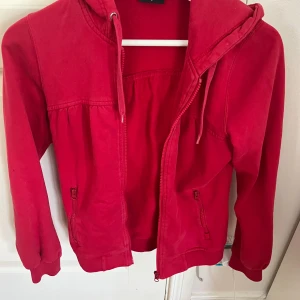 Röd huvtröja från JC - Säljer en snygg röd huvtröja från JC. Tröjan har dragkedja framtill och en praktisk huva med snörning. Perfekt för en avslappnad stil. Den har långa ärmar och är tillverkad i ett mjukt material.