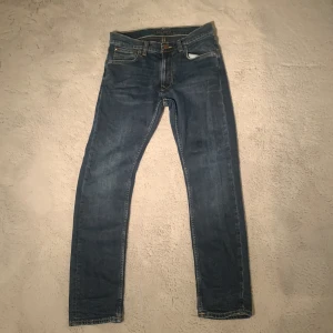 Blå jeans från Nudie Jeans - Snygga blå jeans från Nudie Jeans med klassisk femficksdesign och knappgylf. De har en stilren look med orange sömmar och en bekväm passform men fortfarande slimade. Det är lean dean.