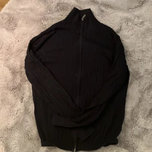 Svart ribbad tröja från Dressmann - Säljer en svart ribbad tröja från Dressmann i storlek S. Tröjan har en dragkedja framtill och är tillverkad i mjuk bomull. Passar bättre M, men sitter också bra på S, tveka inte att höra av er om ni har några funderingar! 