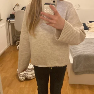 Beige stickad tröja från Gina Tricot - Mysig beige stickad tröja från Gina Tricot. Tröjan har en avslappnad passform med långa ärmar och ribbade muddar vid ärmslut och nederkant. Perfekt för kyligare dagar!