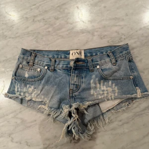 Blå jeansshorts från One Teaspoon - Trendiga ljusblå jeansshorts med slitna detaljer och fransar nedtill. Shortsen har fickor fram och bak, samt en knappgylf. Nypris 1600kr.