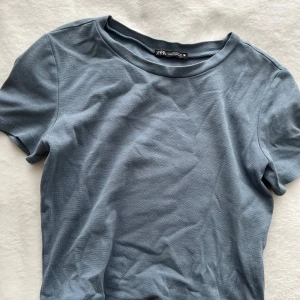 Blå t-shirt från Zara - Säljer en enkel och stilren blå t-shirt från Zara. Den har en rund halsringning och korta ärmar, perfekt för en avslappnad look. Kortare i modellen.