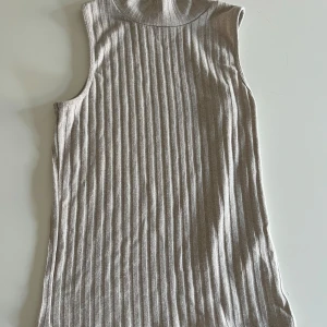 Beige ribbad ärmlös topp - Säljer en stilren beige ribbad topp utan ärmar. Perfekt för lager-på-lager eller att bära som den är. Den har en hög krage och är tillverkad i ett mjukt material som ger en skön passform. Pris kan diskuteras!💕