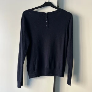 Mörkblå långärmad tröja från H&M - Säljer en stilren mörkblå finstickad långärmad tröja från H&M. Tröjan har en rund halsringning och knappar på baksidan. Perfekt för en enkel och elegant look.