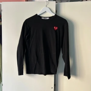 Svart långärmad tröja från Comme des Garçons - Säljer en stilren svart långärmad tröja från Comme des Garçons. Perfekt för en minimalistisk look.