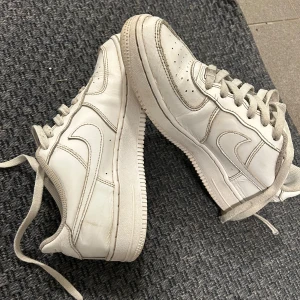 Vita Nike Air Force sneakers - Säljer ett par klassiska vita Nike Air Force sneakers. De har en stilren design med snörning och den ikoniska swoosh-loggan på sidan. Perfekta för en casual look.