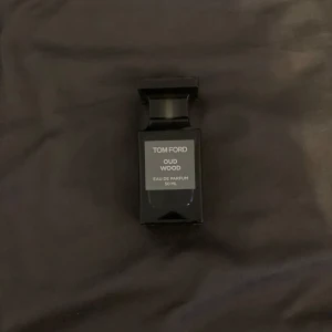 Tom Ford Oud Wood Eau de Parfum - Exklusiv och elegant parfym från Tom Ford, Oud Wood, i en stilren svart flaska. Doften är känd för sina rika och träiga noter, perfekt för den som söker en sofistikerad och unik doftupplevelse. Flaskan rymmer 50 ml av denna lyxiga parfym. Låda finns med till parfymen.