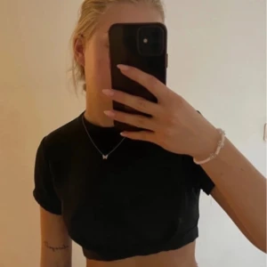 Svart croppad topp med öppen rygg - Säljer en svart croppad topp med korta ärmar och snygg öppen rygg. Toppen har en knytning baktill och passar perfekt till både jeans och kjol. Enkel och stilren design.