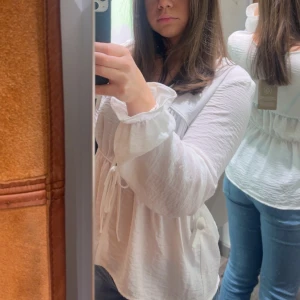 Vit blus med knytning - Säljer en vit blus från AWARE med v-ringning och knytning framtill. Blusen har långa ärmar med resår vid ärmslut och en lätt rynkad midja för en feminin siluett. Perfekt till vardags och till lite mer festligare. 