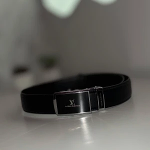 Svart Bälte Från Välkänt Märke - Stilrent svart bälte från välkänt varumärke med exklusivt silverfärgat spänne. Bältet är tillverkat i skinn och har en elegant design med diskret logotyp på spännet. Perfekt accessoar för att lyfta din outfit.