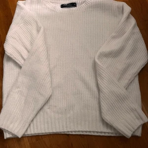 Vit ribbad stickad tröja - Säljer en vit stickad tröja med ribbad struktur och rund halsringning. Tröjan har långa ärmar och en klassisk, enkel design som passar perfekt till många olika outfits.
