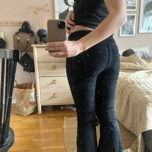 Svarta bootcut jeans - Säljer ett par svarta bootcut jeans med normal passform och sametslikande material. Jeansen har klassisk femficksdesign, dragkedja och knapp framtill. Perfekta för dig som gillar en tidlös look med lite utsvängda ben.