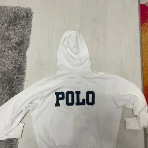 Hodie från Polo Ralph Lauren - Säljer en skön vit ralph lauren hoodie med Unisex hoodie. vit hoodie med tryck på ryggen. Den har en liten svart sträck på botten delen och vid sidan men syns knappast och kan nog tas bort. Den i xs/barn Large. 
