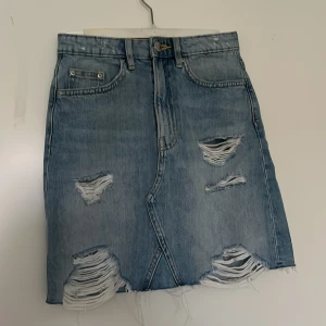 Blå jeanskjol med slitningar från H&M Divided - Säljer en blå jeanskjol från H&M Divided med coola slitningar väl använd.🤍