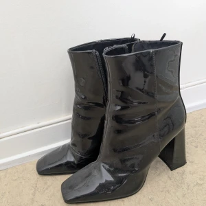 Svarta lackade boots med klack - Säljer ett par svarta boots i glansigt lackmaterial med hög klack och fyrkantig tå. Skorna har dragkedja på insidan för enkel påtagning och en stilren, modern look. Använda en gång. 