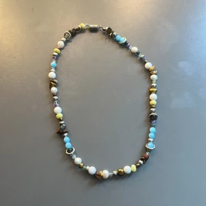Färgglatt pärlhalsband med blandade stenar - Handgjort halsband med pärlor i olika färger som blått, vitt, gult och brunt. Halsbandet har både runda och oregelbundna pärlor samt detaljer i metall. 