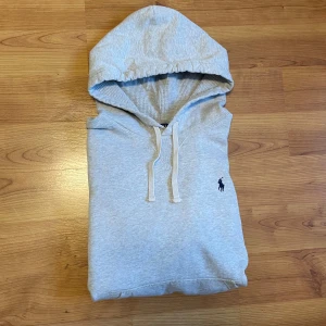 Grå hoodie från Polo Ralph Lauren - Säljer en stilren ljusgrå hoodie från Polo Ralph Lauren med klassisk huva och dragsnören. Tröjan är i mycket bra skick utan några defekter