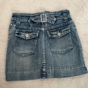 Jeanskjol - Säljer en snygg jeanskjol från Xhilaration i klassisk blå denim. Kjolen har två stora fickor med knappar bak och ett matchande bälte i midjan. Perfekt för dig som gillar en cool och avslappnad stil. Det står att den är i storlek M men jag skulle säga att den är i xxs/xs