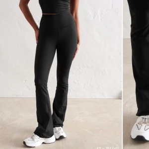 Svarta bootcut leggings från Aim'n - Svarta höga leggings från Aim'n med bootcut-passform. Byxorna har bred resår i midjan och är tillverkade i ett stretchigt syntetmaterial som sitter tight upptill och släpper ut vid bensluten. Perfekta för träning eller en sportig look. ordinarie pris 1298