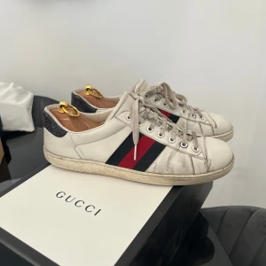 Gucci sneakers med röd och marinblå rand - Säljer ett par klassiska vita Gucci sneakers med signaturränder i rött och marinblått på sidorna. Lägg till nya snören för fräschare look.