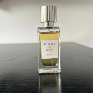 Eight & Bob Egypt Eau de Parfum - Exklusiv parfym från Eight & Bob med namnet Egypt. Flaskan är rektangulär i genomskinligt glas med en silverfärgad metallkork. Parfymen har en gyllengul nyans och en stilren etikett framtill.