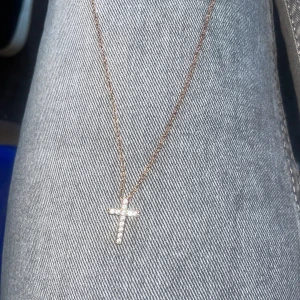 Halsband med korshänge i guld och stenar - Säljer ett elegant halsband med ett korsformat hänge i guldton, dekorerat med gnistrande stenar. Kedjan är tunn och smidig, perfekt för att ge en stilren touch till din outfit. Köpt i USA  2024