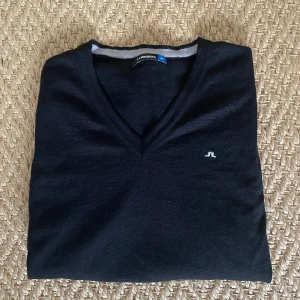 Svart v-ringad tröja från J.Lindeberg - OBS! Står M men skulle säga det är S annars Säljer en svart v-ringad tröja från J.Lindeberg med diskret logga på bröstet. Tröjan har långa ärmar och ribbade muddar vid ärmslut och nederkant. Perfekt för en stilren och enkel look.