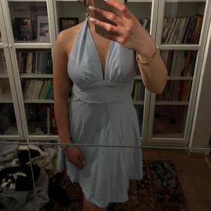 Ljusblå halterneckklänning - Säljer en ljusblå klänning med halterneck och v-ringning. Klänningen har en markerad midja och ett lätt utställt kjolparti som ger en feminin siluett. Perfekt för sommarens tillfällen! Skräddarsydd, passar mig med S perfekt.