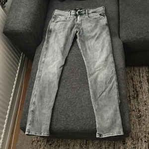 Grå Replay Anbass jeans - Säljer ett par gråa Replay Hyperflex Anbass jeans med tvättad look och klassiska fem fickor. Byxorna har normal passform och raka ben, med Replay-logga på bakfickan och vid fickan fram. Perfekta för dig som gillar stilrena jeans med snygga detaljer. Säljes för 550 bara använda max 5 par gånger. Priset är ej hugget i sten. 