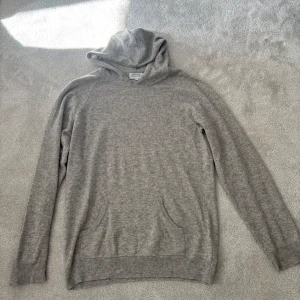 Grå hoodie i kashmir från Davida - Mjuk och lyxig grå hoodie från Davida i kashmir. Tröjan har långa ärmar, huva och en praktisk magficka framtill. Perfekt för en avslappnad och stilren look.