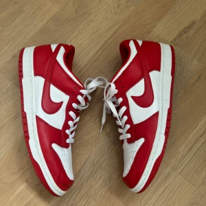 Nike Dunk Low University Red – EU44.5 / US10.5 (Classic Colorway) - Stilrena Nike Dunk Low i den klassiska “University Red”-färgen – röd och vit i skön retrolook. En ikonisk sneaker som funkar året runt och är lätt att matcha. 	•	Storlek: EU 44.5 / US 10.5 / UK 9.5 	•	Modellkod: CU1727-100 	•	Färg: University Red / White