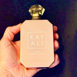 Kayali Utopia Vanilla Coco | 21 Eau de Parfum - Lyxig parfymflaska i ljusrosa med guldiga detaljer och en kristalliknande kork. Doften Utopia Vanilla Coco | 21 kombinerar vanilj och kokos för en varm, söt och fräsch känsla. Perfekt för dig som älskar mjuka och krämiga doftnoter. 100 ml, endast testad. 