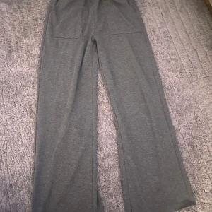 Grå mjukisbyxor med raka ben - Mysiga grå mjukisbyxor med bred resår i midjan och raka, vida ben. Byxorna har två stora fickor framtill och är perfekta för en avslappnad stil. Passar lika bra hemma som till en chill vardagslook.