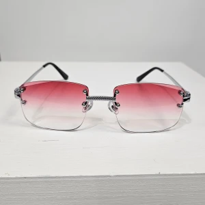 Rektangulära solglasögon med rosa tonade glas - Snygga solglasögon med rektangulära, kantiga glas i en rosa tonad färg som övergår till transparent. Metallbågar med svarta skalmar ger en modern och stilren look. Perfekta för dig som vill sticka ut med en trendig accessoar.