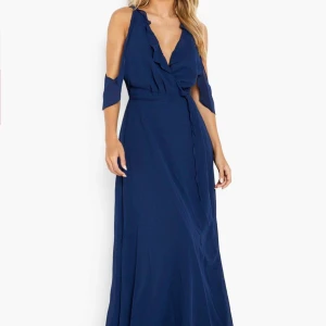 Marinblå långklänning med volang och v-ringning - Säljer en marinblå långklänning med v-ringning och volangdetaljer. Klänningen har offshoulder-ärmar och omlottkänsla framtill. Perfekt för bal eller fest. Materialet känns lätt och luftigt. Aldrig använt och har prislapp kvar. 