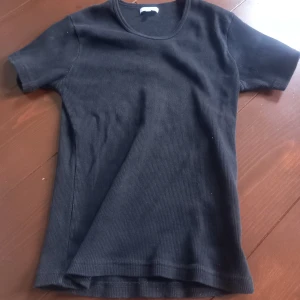 Svart ribbad t-shirt - En svart ribbad t-shirt med rund halsringning och korta ärmar. Enkel och stilren modell som passar perfekt till jeans eller kjol. Materialet är stretchigt och bekvämt.