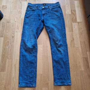 Blå jeansbyxor från Lee - Säljer ett par klassiska blå jeans från Lee i rak passform. Byxorna har fem fickor, gylf med dragkedja och knapp samt Lee-logga på bakfickan. Perfekta för dig som gillar tidlös denimstil.