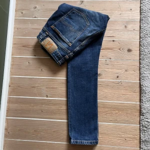 Blå jeans från Nudie Jeans modell skinny Lin, W27 L28  - Säljer ett par klassiska blå Nudie jeans, modell Skinny Lin. med snygg tvätt och orangea sömmar. Använda men inga skavanker vad jag kan se. Perfekta till sneakers och funkar året runt.