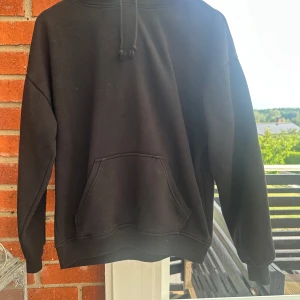 Svart hoodie med magficka XS - En klassisk svart hoodie med huva och snörning. Tröjan har en stor magficka framtill och ribbade muddar vid ärmslut och nederkant. Storlek XS från BikBok