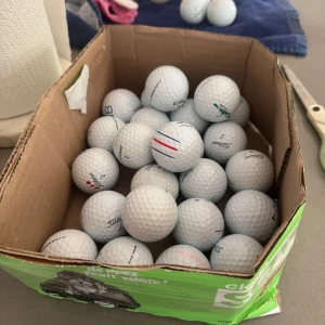 Golfbollar coola bollar 12 st - Den här bilden visar en kartong fylld med golfbollar av olika märken, bland annat Titleist och Callaway. Perfekt för dig som vill fylla på golfbagen inför säsongen eller testa nya bollar på banan. Passar både nybörjare och erfarna golfare.
