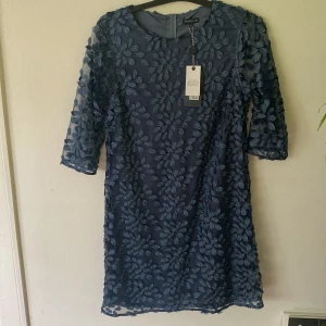 Blå blommig kortklänning Stockh LM - Superfin blå kortklänning från Stockh LM med 3D-blommor över hela klänningen. Halvlånga ärmar och dragkedja bak. Modellen heter Verona dress och har en elegant, figurnära passform. Perfekt för dig som vill sticka ut med en unik look. Helt ny med prislappen kvar, aldrig använd endast testad. Nypris -799kr