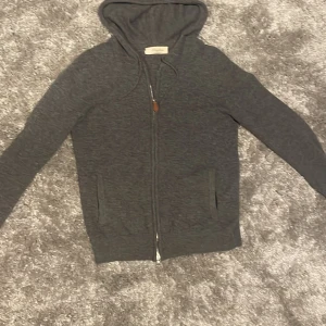 Mörkgrå kashmir hoodie - Mörkgrå hoodie från Sofillin med hel dragkedja framtill, huva med snörning och två fickor. Tröjan är långärmad och har en avslappnad passform, perfekt för chill dagar. Materialet känns mjukt och skönt mot huden.